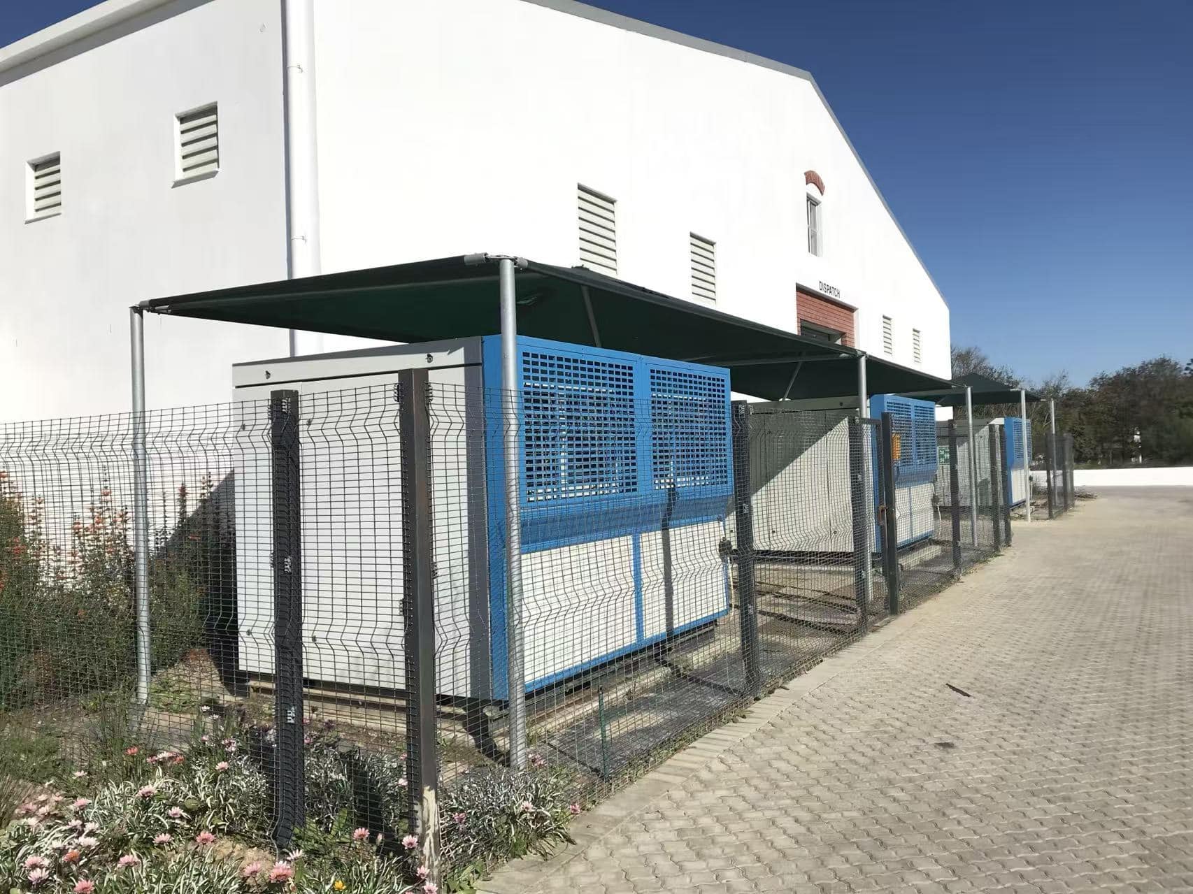 Row of ZENIUS 2,000 L/day atmospheric water generators installed outdoors under individual shade canopies behind a security fence at a customer bottling plant